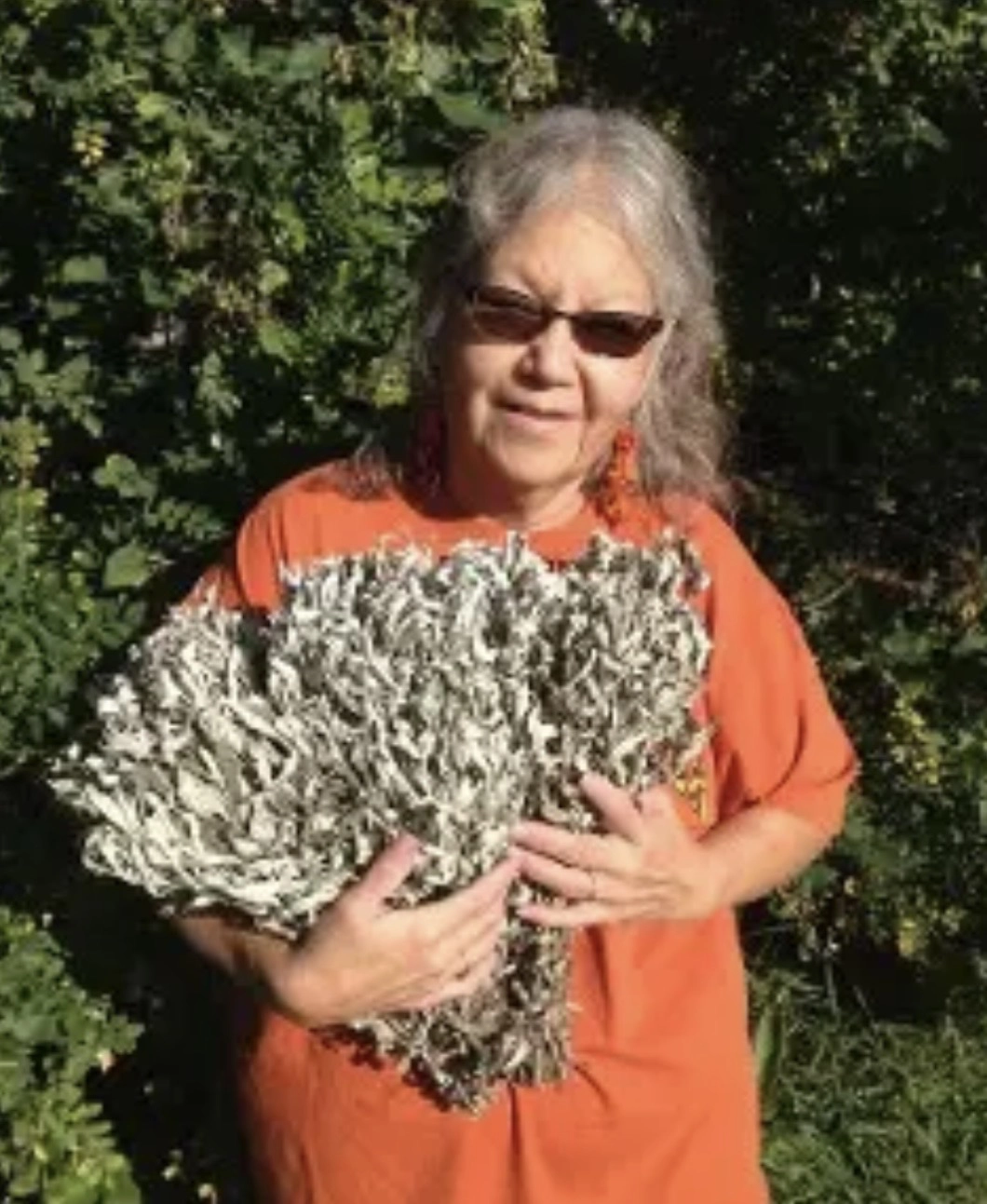 Colleen standing outdoors holding a bundle of dried greenery.